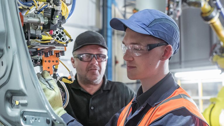 Apprentice engineer with mentor and robots in car factory - stock photo