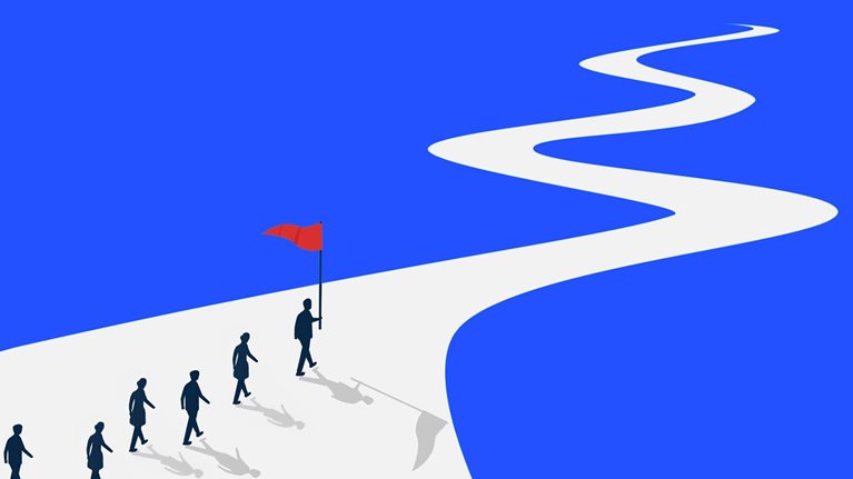 An illustration of six silhouetted people walking along a wide white winding path on a bright blue background, with the person in front carrying a red flag.