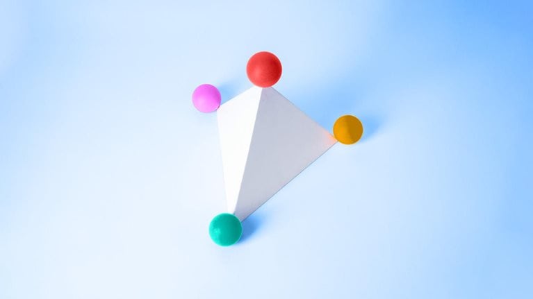 A white triangular pyramid with four balls of varying colors situated at each of the pyramid's points. 