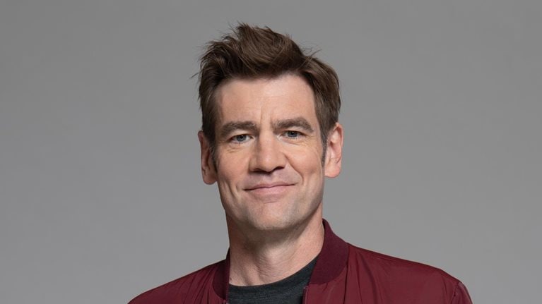  Portrait of Chris Dixon with a light smile against a gray backdrop.