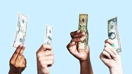 A diverse group of hands holding up US dollar banknotes of various denominations on light blue background.