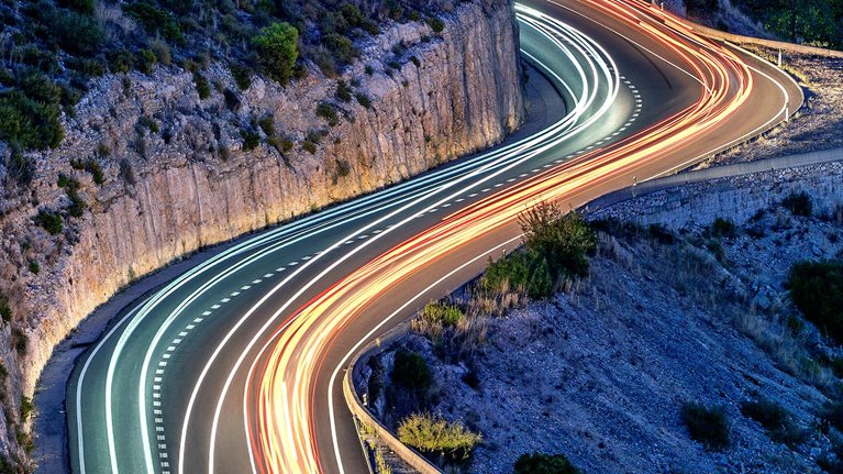 A high angle of a light trails on a s-shaped mountain road at night between the towns of Bocairent and Ontinyent.