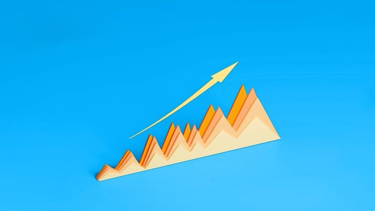 A three-dimensional graph made of paper displays a positive trend with its peaks and valleys. A gold arrow follows the upward trajectory of the graph against a vibrant blue background.