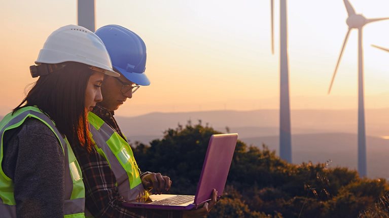 Engineers with Safety Helmets and Vests Using Laptop at Wind Farm During Sunset, Highlighting Renewable Energy, Sustainability, and Green Technology Innovation