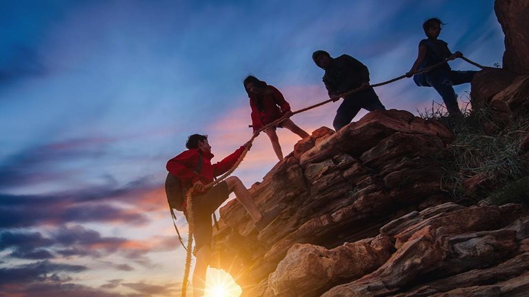 Hikers climbing up on the mountain at sunset ,teamwork and helping concept.