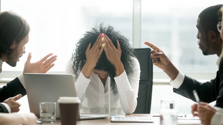 A woman with her hands over her head expressing frustration during a conference meeting with colleagues