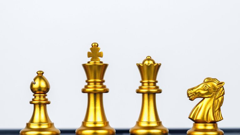 Six golden chess pieces stand proudly in a row on the board. From left to right, we have a pawn, a bishop, a knight, a king, a queen, and a rook.