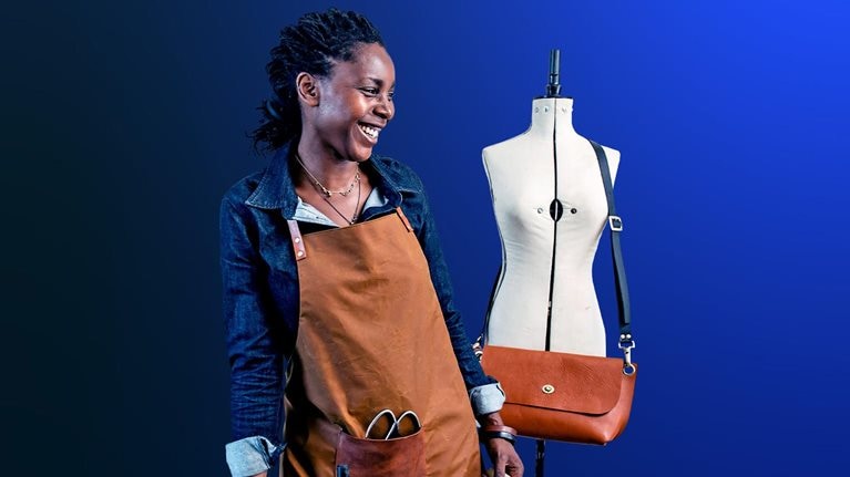 An image of a small business owner sharing a laugh at her design studio, where she makes leather goods to sell in her shop.