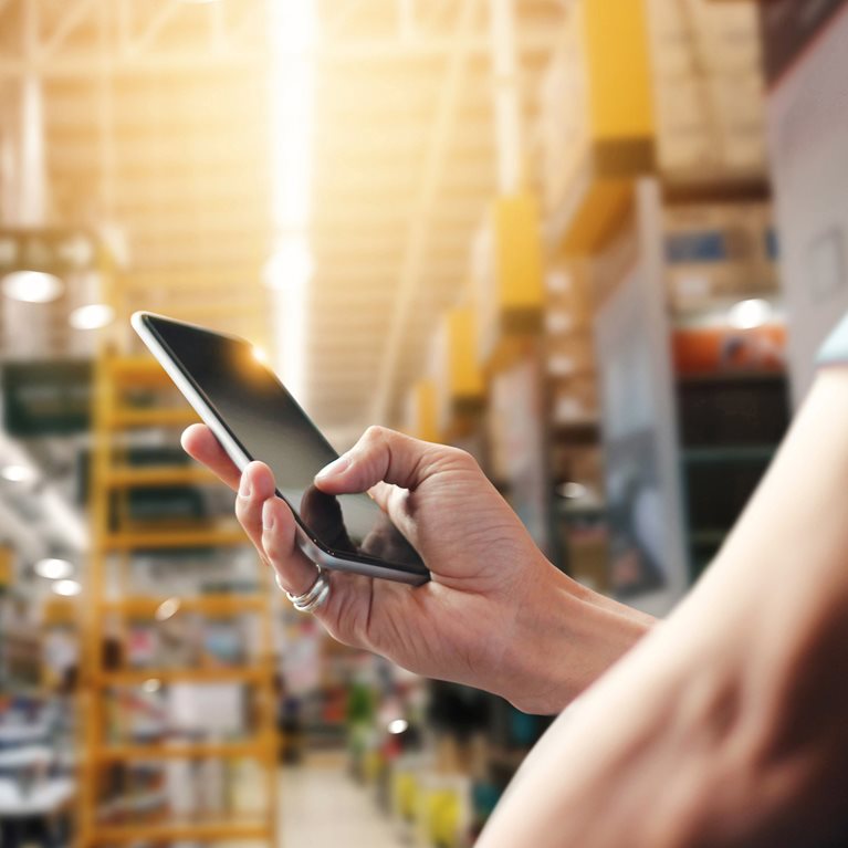 A worker consults a mobile phone in a warehouse full of goods
