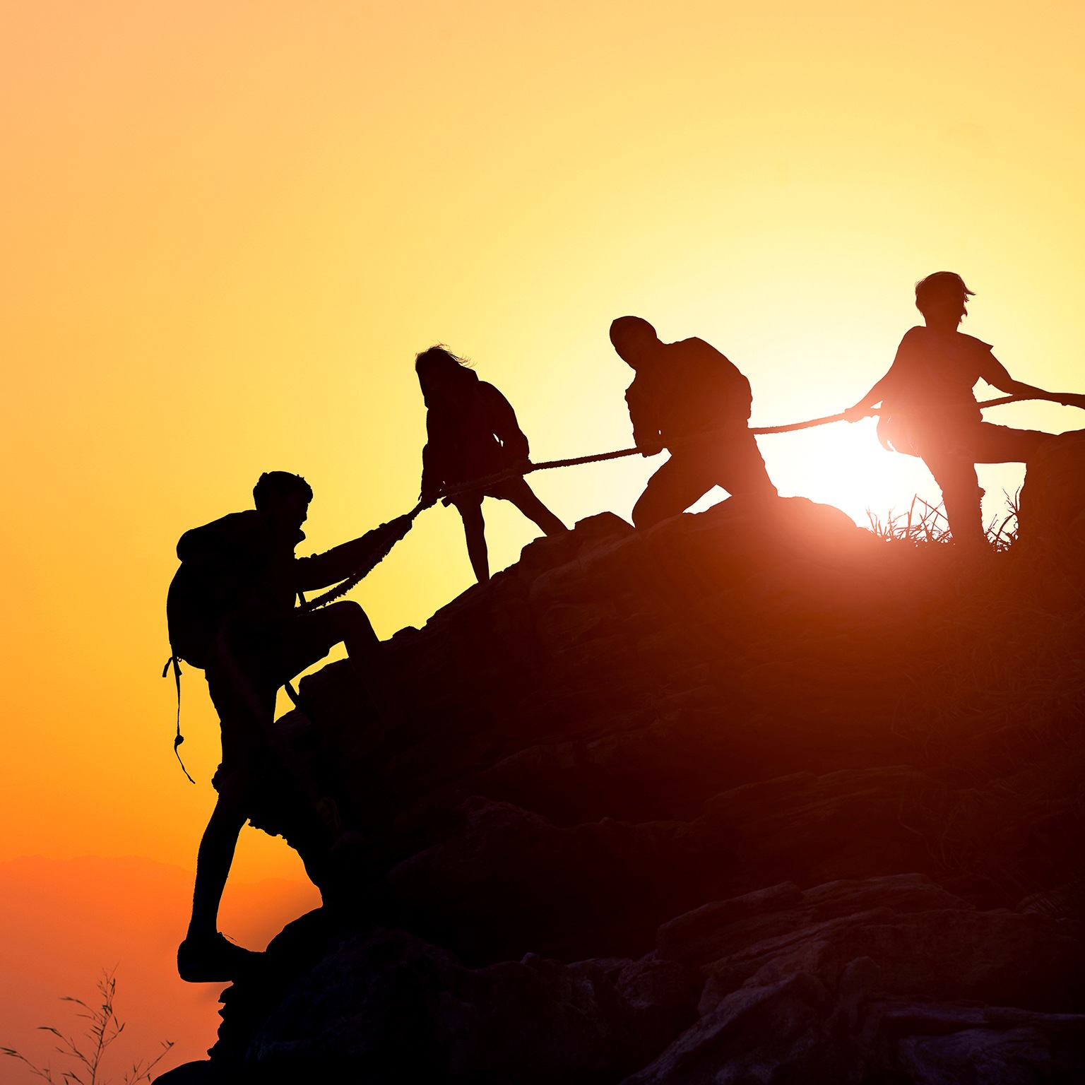 Silhouette of the climbing team helping each other while climbing up in a sunset
