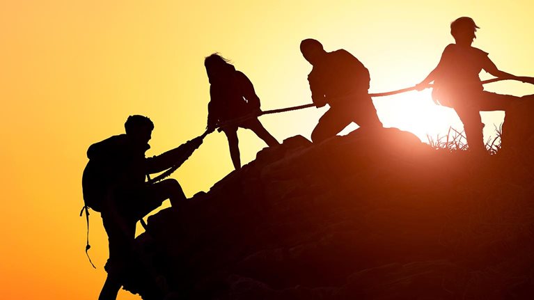 Silhouette of the climbing team helping each other while climbing up in a sunset