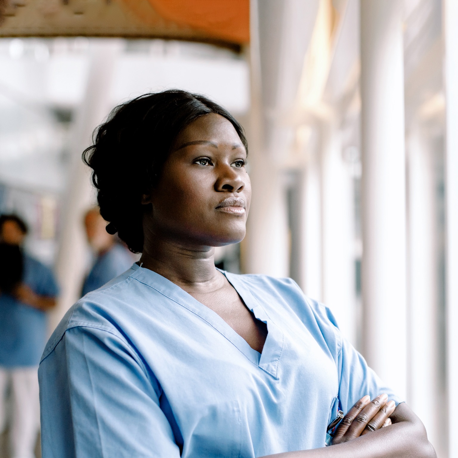 Contemplating female nurse with arms crossed looking through window in hospital
