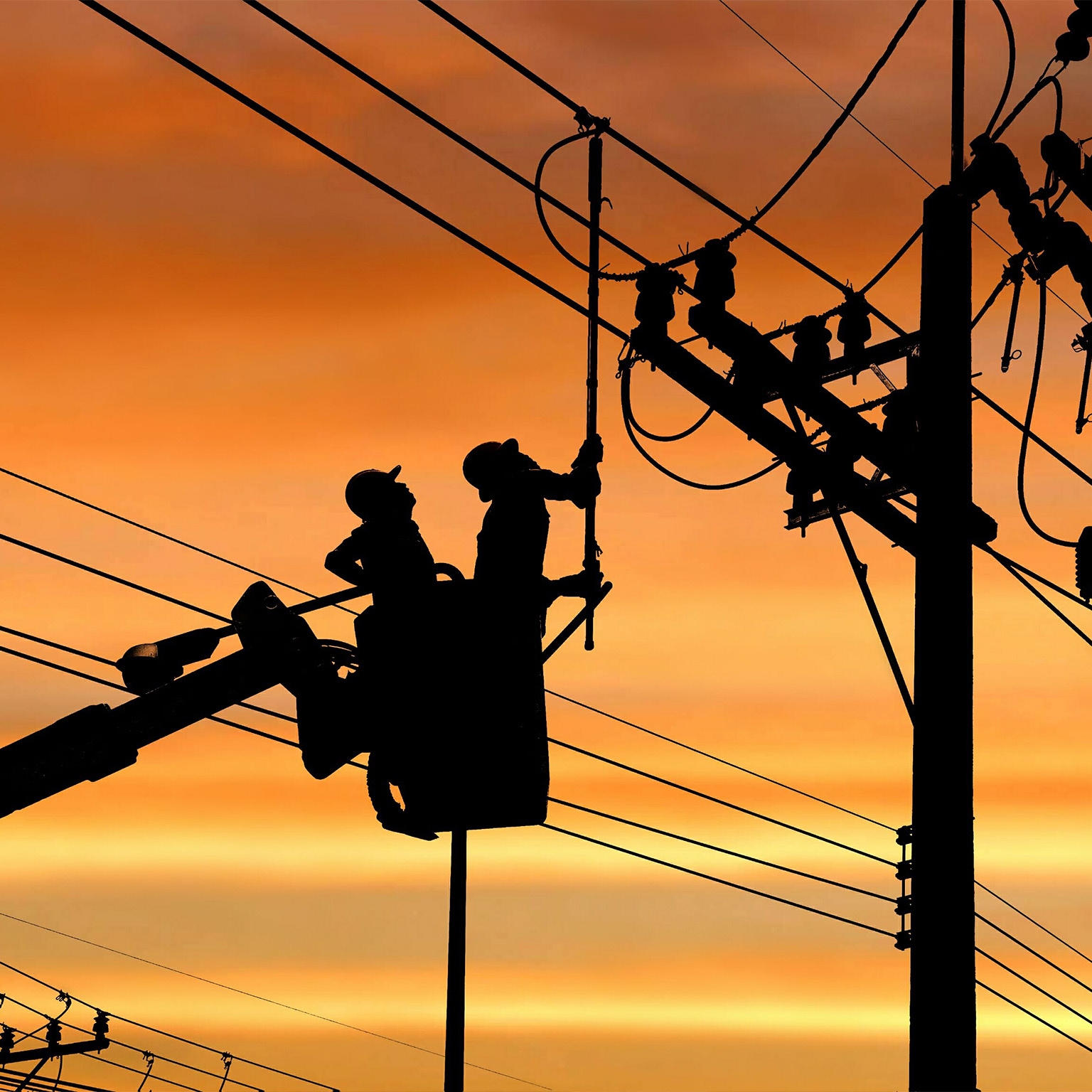 Silhouette two electricians with disconnect stick tool on crane truck are working to install electrical transmission on power pole - stock photo
