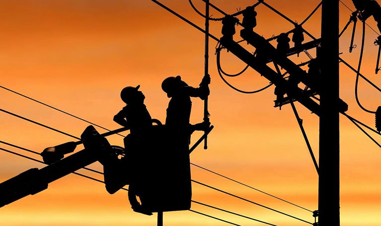 Silhouette two electricians with disconnect stick tool on crane truck are working to install electrical transmission on power pole - stock photo