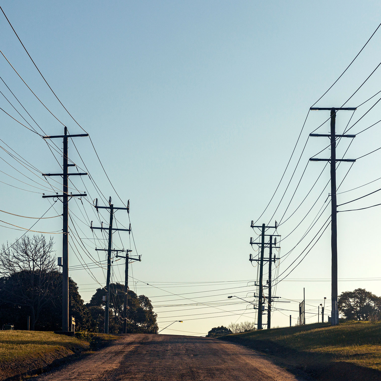 Electric poles with many cables located along rural country road with clear blue sky in background