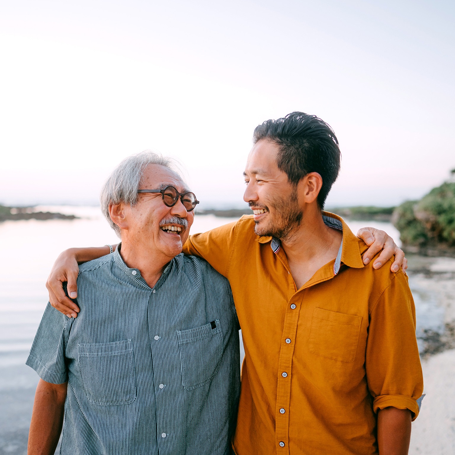 Senior father and adult son having a good time on beach at sunset