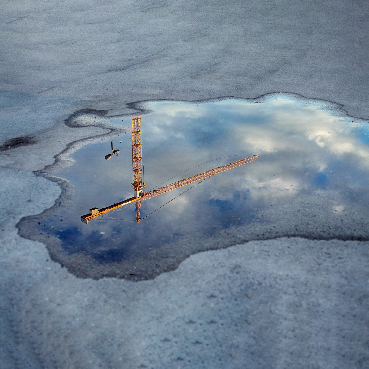 Reflection of a crane tower in a puddle