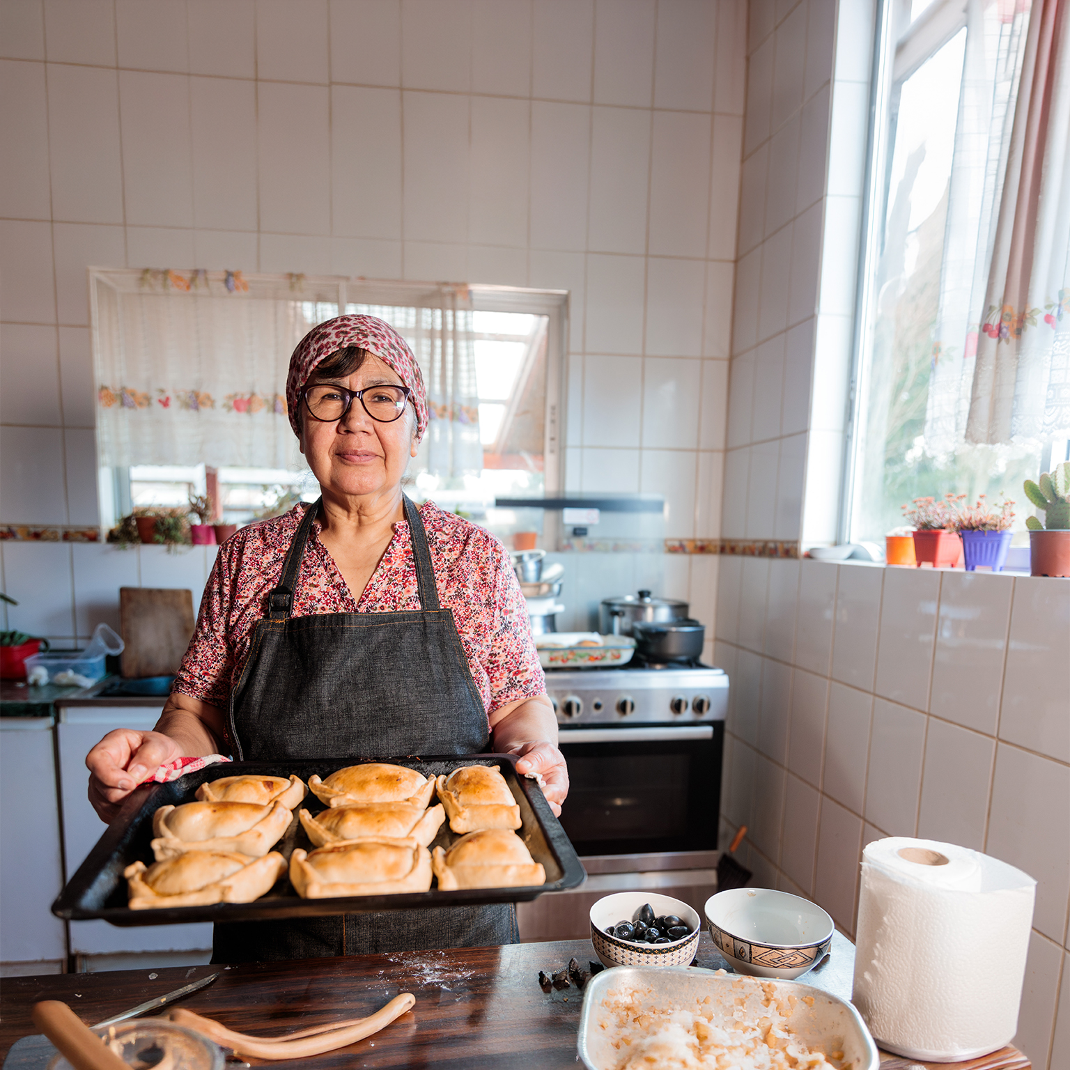 Latin elderly woman preparing Chilean baked beef empanadas in her home kitchen