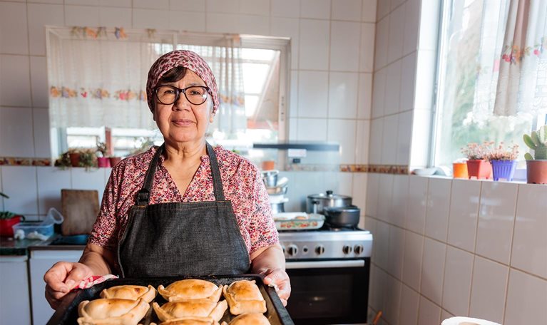 Latin elderly woman preparing Chilean baked beef empanadas in her home kitchen