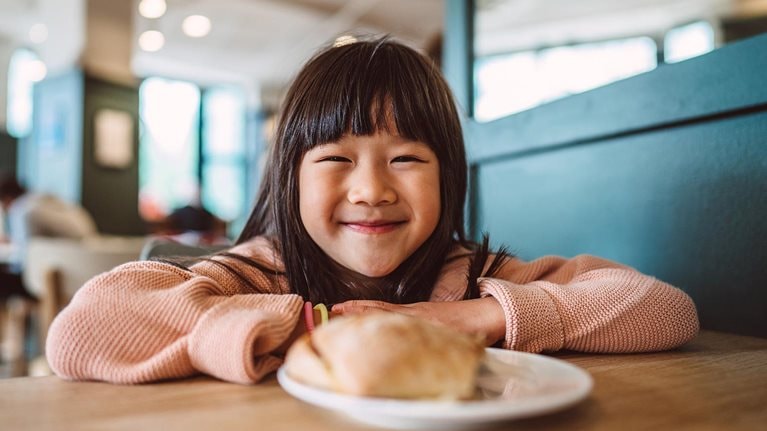 Lovely cheerful girl smiling joyfully at the camera while enjoying meal in a cafe.