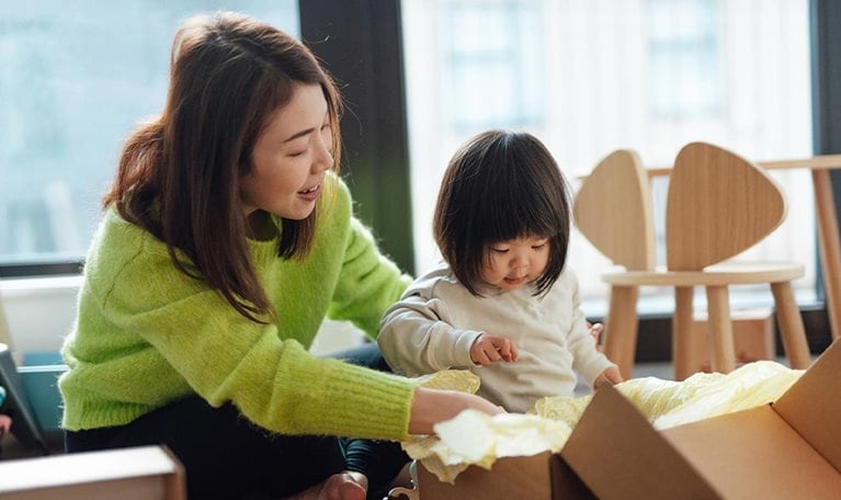 Young Asian mother unpacking parcel from online shopping with her toddler