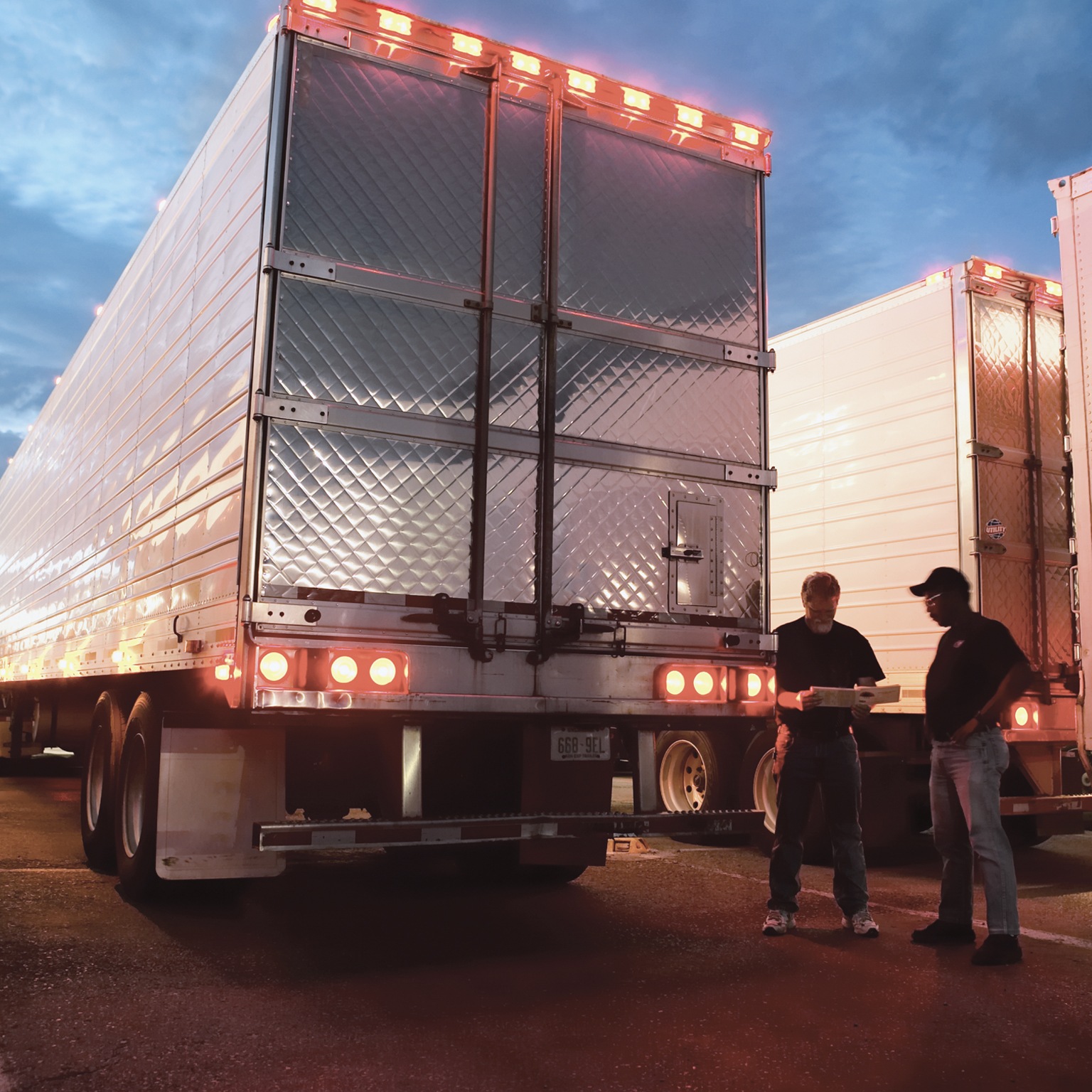 Two truck drivers standing next to truck trailers