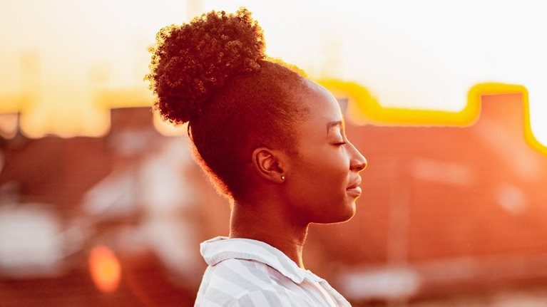 Young African American woman is relaxing on the rooftop with sunset light on her face