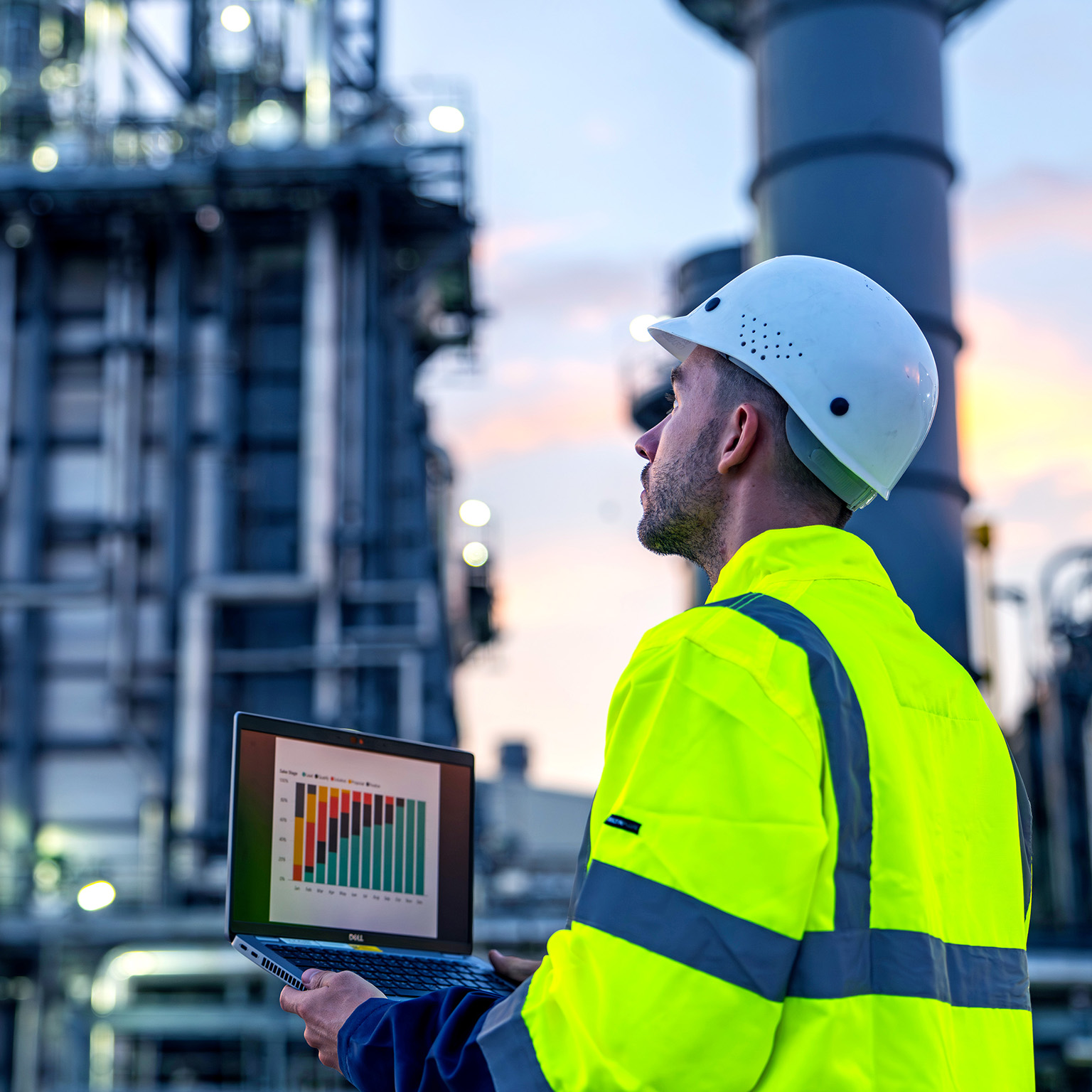 An industrial engineer using a laptop to monitor operational data at a facility. 