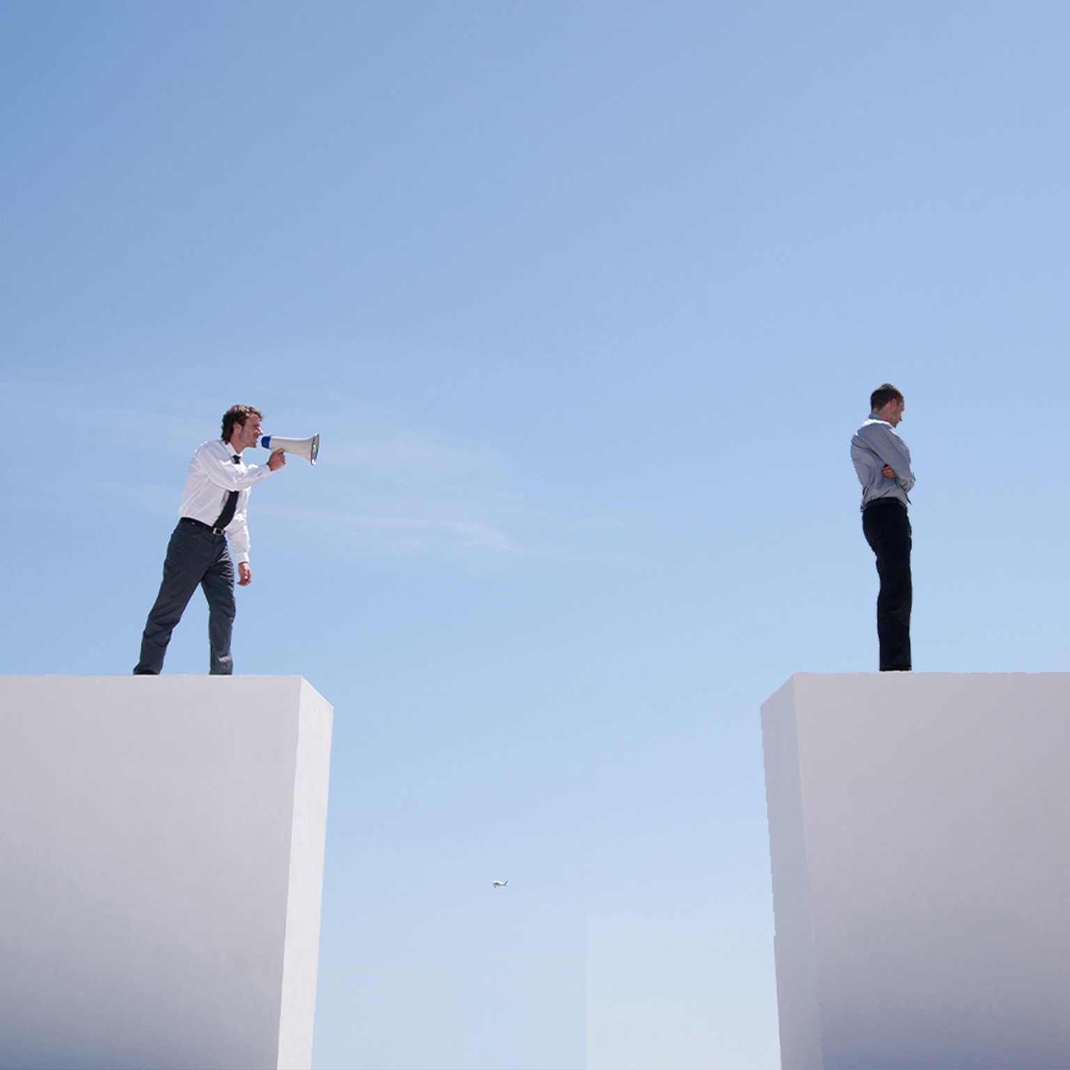 Businessman with megaphone on wall shouting at businessman on wall with gap