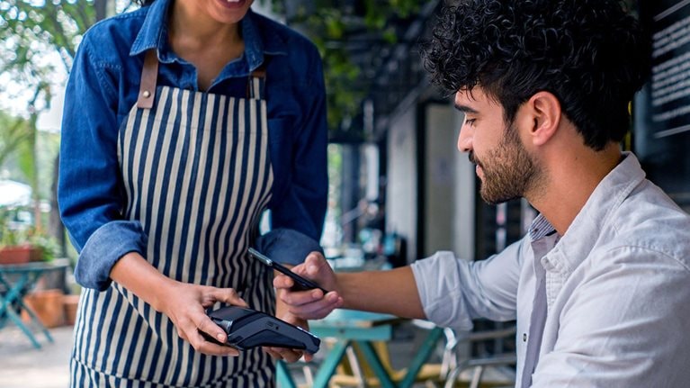 Latin American man making a contactless payment to the waitress at a restaurant using his cell phone