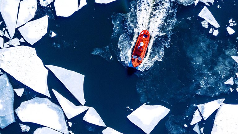 Wintery aerial view of a red ice-breaker ship pushing through cracked sea ice
