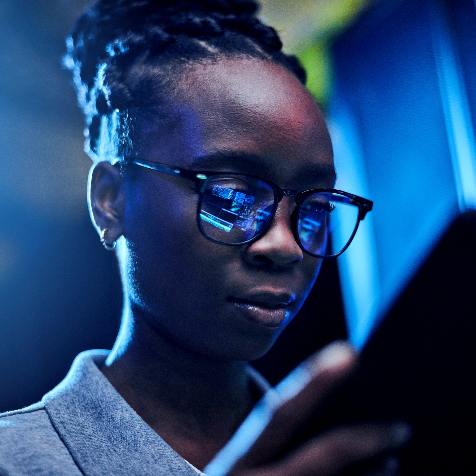 Engineer using a digital tablet while working in a server room with code reflected in her glasses.