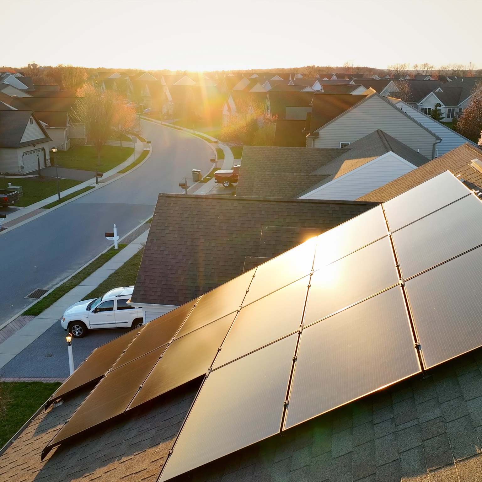 Aerial close up of modern house with solar array reflecting golden hour sunlight.