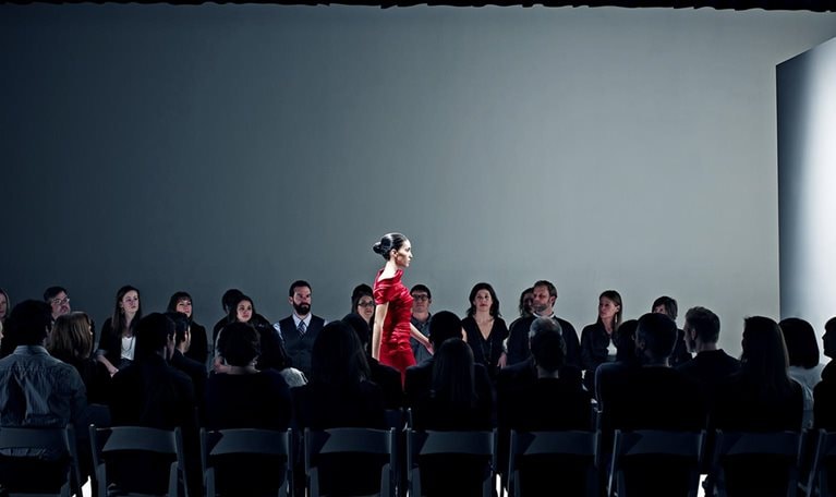 Female model walking on catwalk in front of crowd at fashion show.