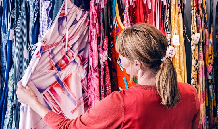 Woman looking at dress hanging on rack while standing in store