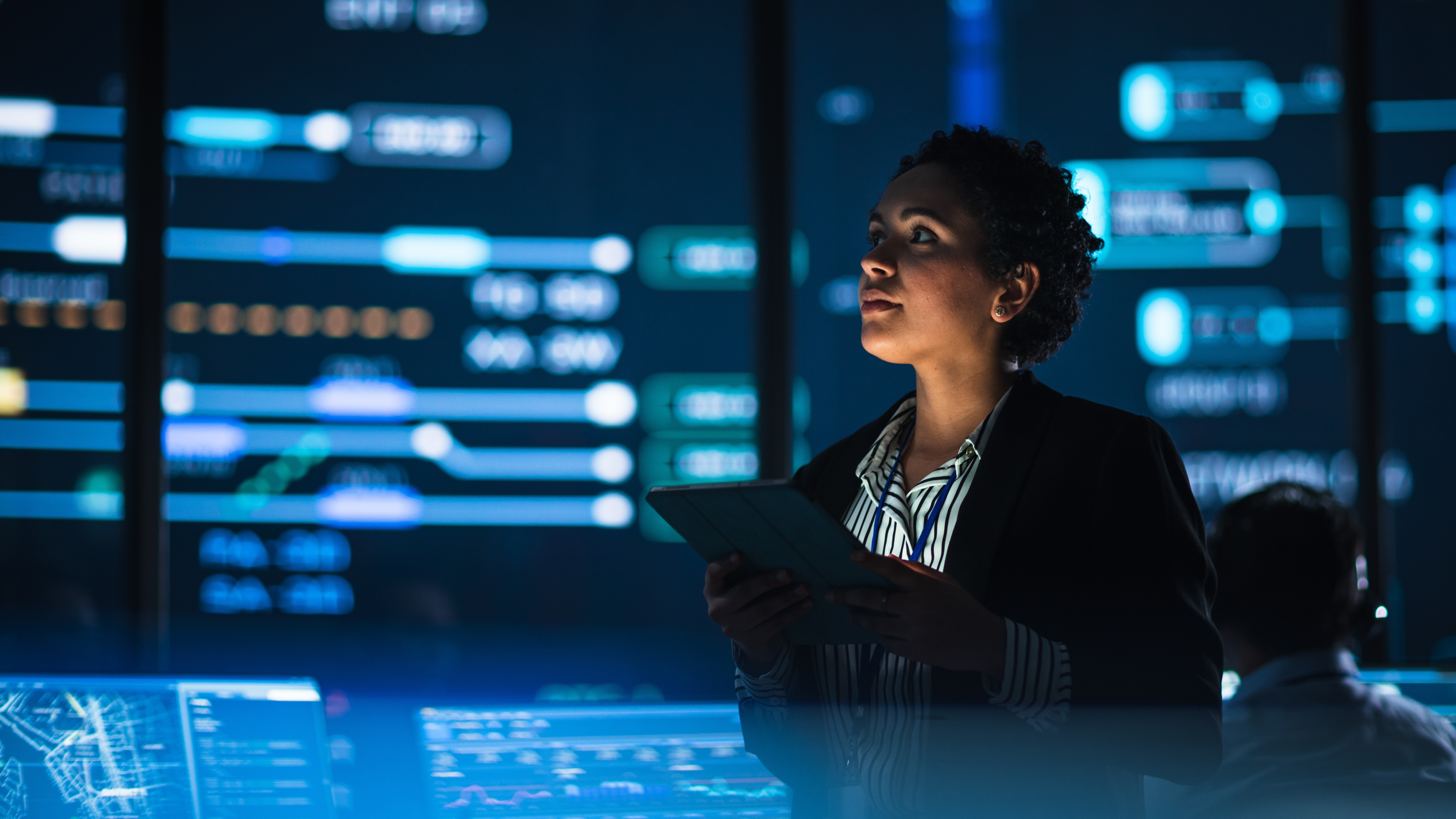 Government Employee Uses Tablet Computer in System Control Monitoring Center. In the Background Her Coworkers at Their Workspaces with Many Displays Showing Technical Data.