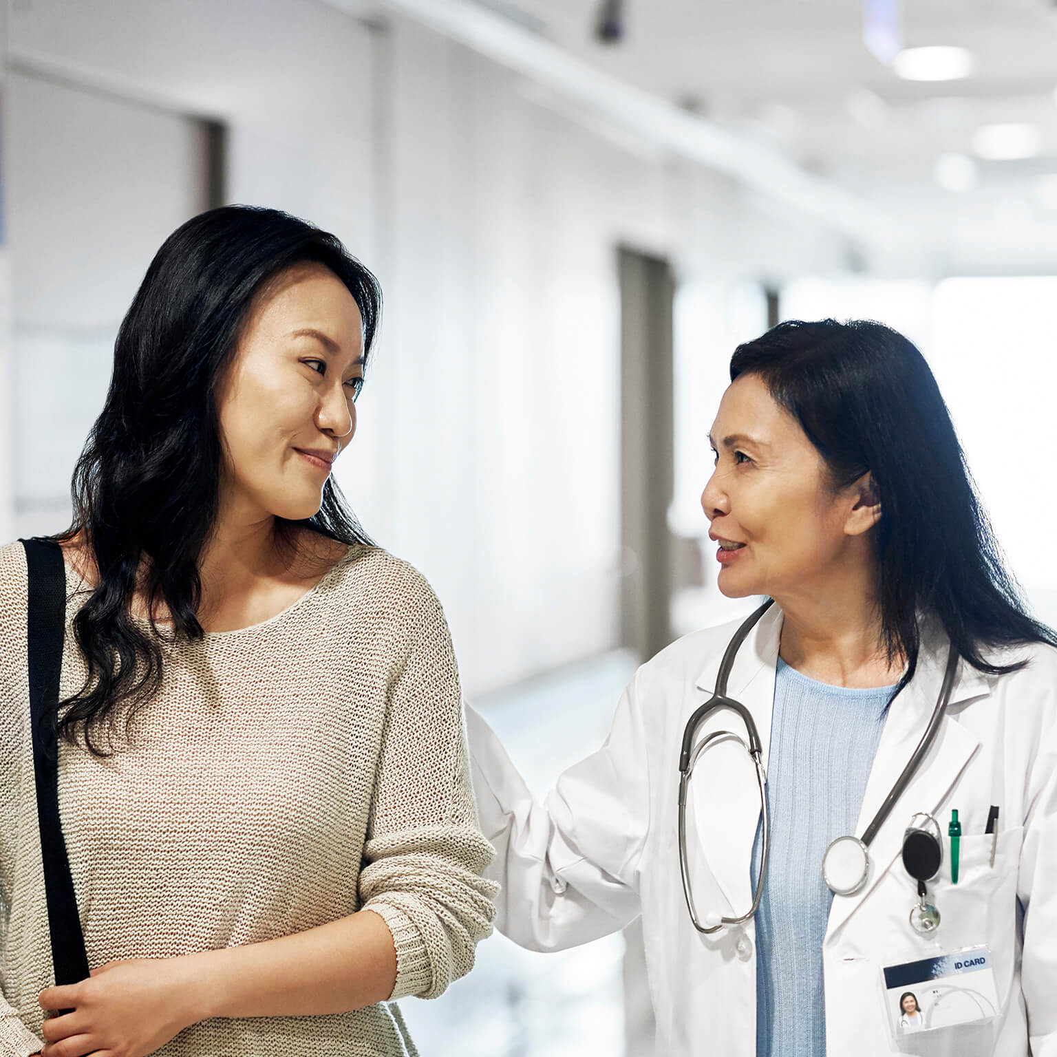 woman doctor comforting woman patient walking down hospital hallway