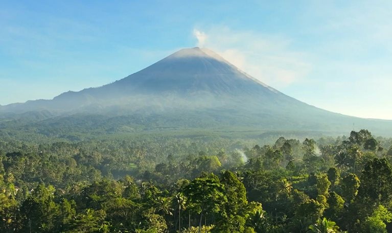 Scenic aerial view sunrise scene of Tumpak Sewu waterfall with Semeru Volcano Background with the jungles on Java Island, Indonesia.