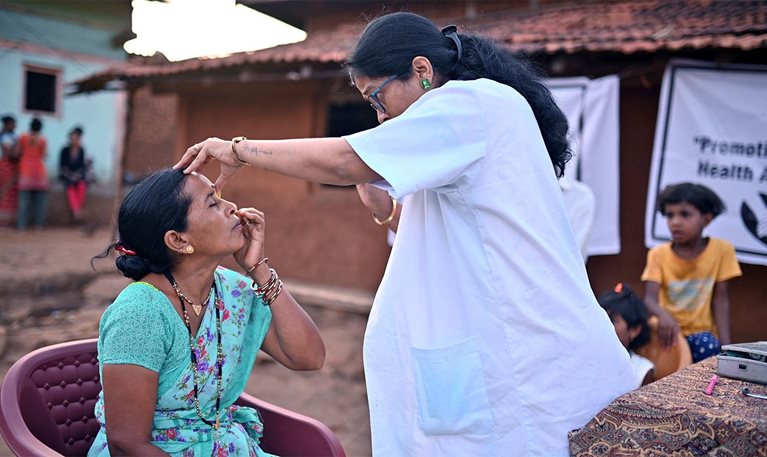 Doctor conducts an eye examination of a mid adult woman during a rural medical health care camp