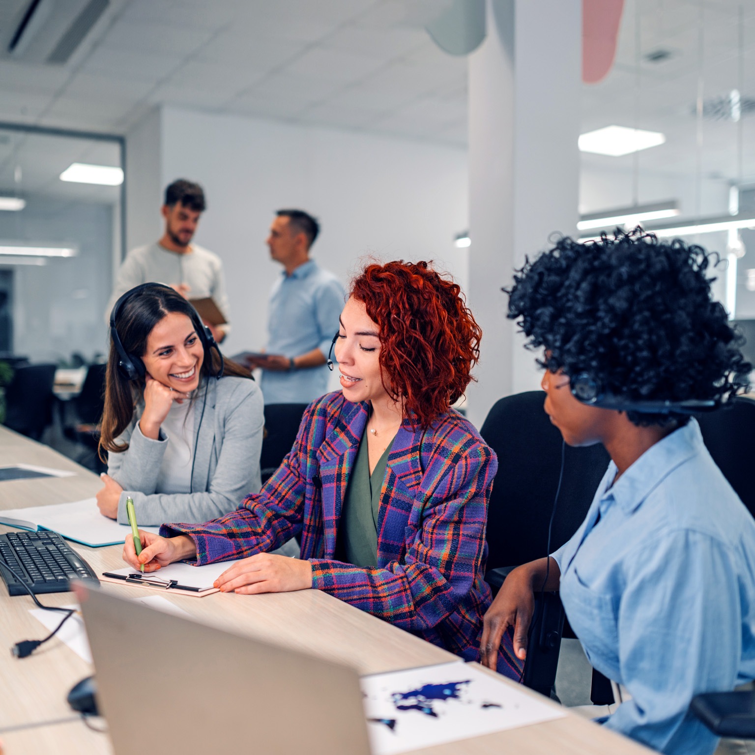 A technical support manager at a call center sits in between two colleagues as she instructs them on how to assist customers.