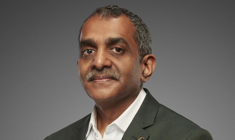 A portrait of Vijay Anand Guntur shows him wearing a gray suit jacket and a white button down shirt, exuding confidence with his gaze. He has well-groomed salt-and-pepper hair and a mustache.