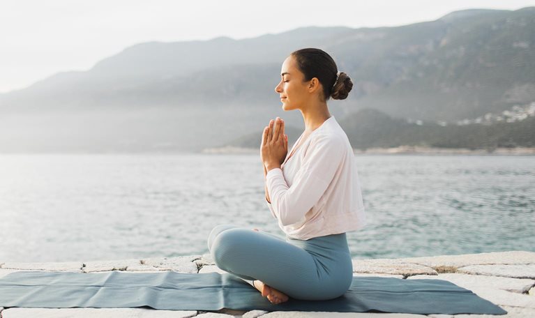 Young woman praying and meditating outdoors by seaside.