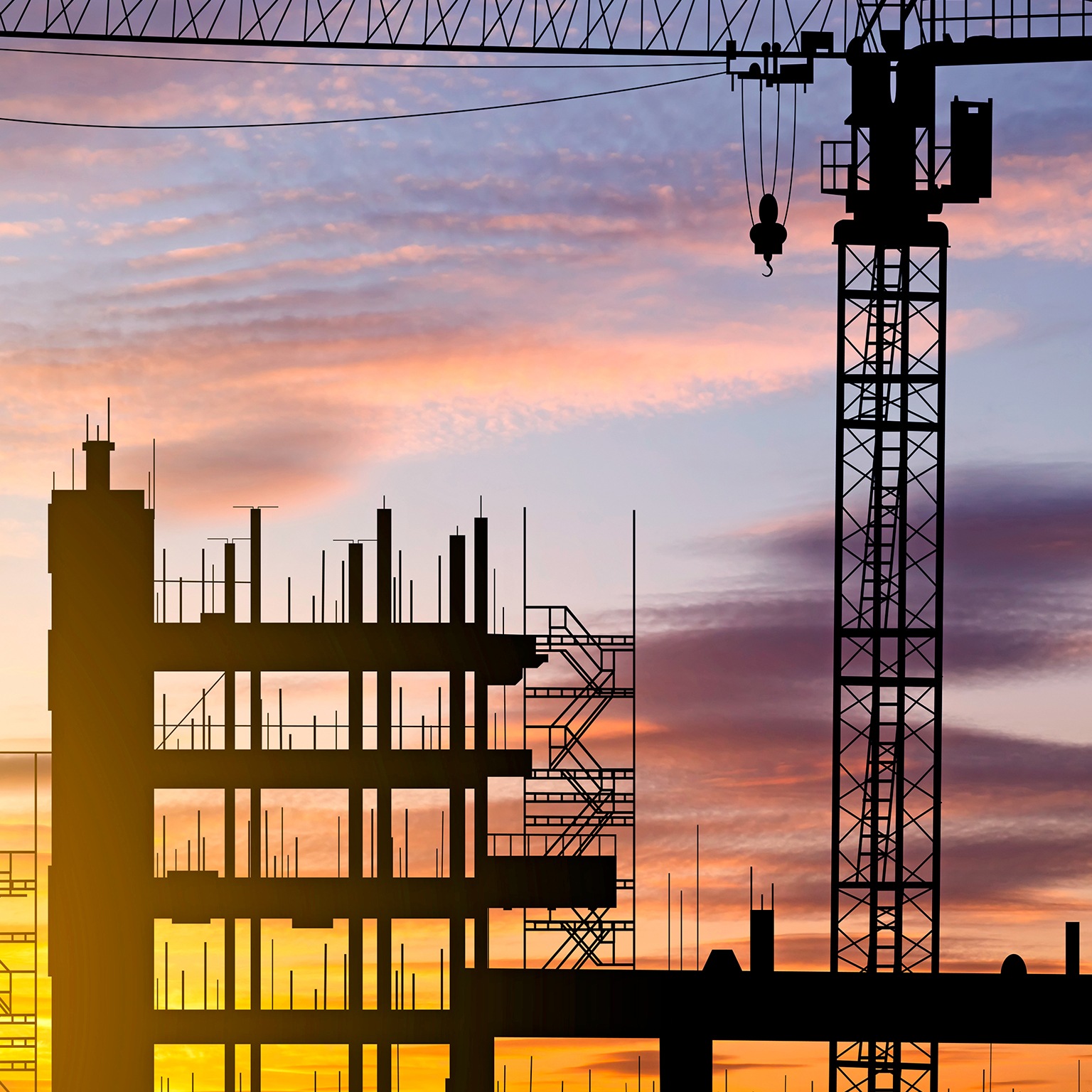 A skyline view of a construction site with cranes at sunset during construction of an apartment building