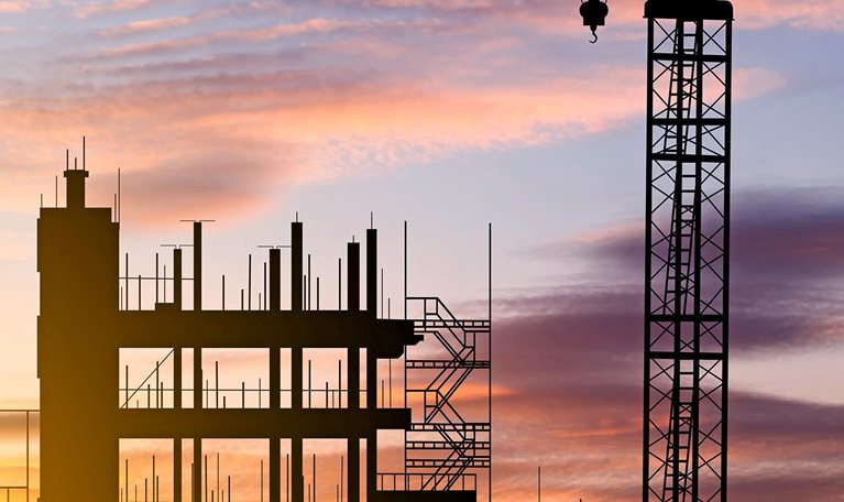 A skyline view of a construction site with cranes at sunset during construction of an apartment building