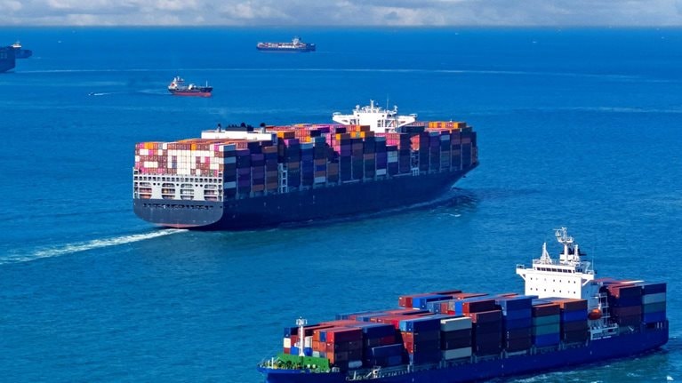 An image of several container ships navigating a vast expanse of blue ocean under a sky filled with fluffy white clouds.