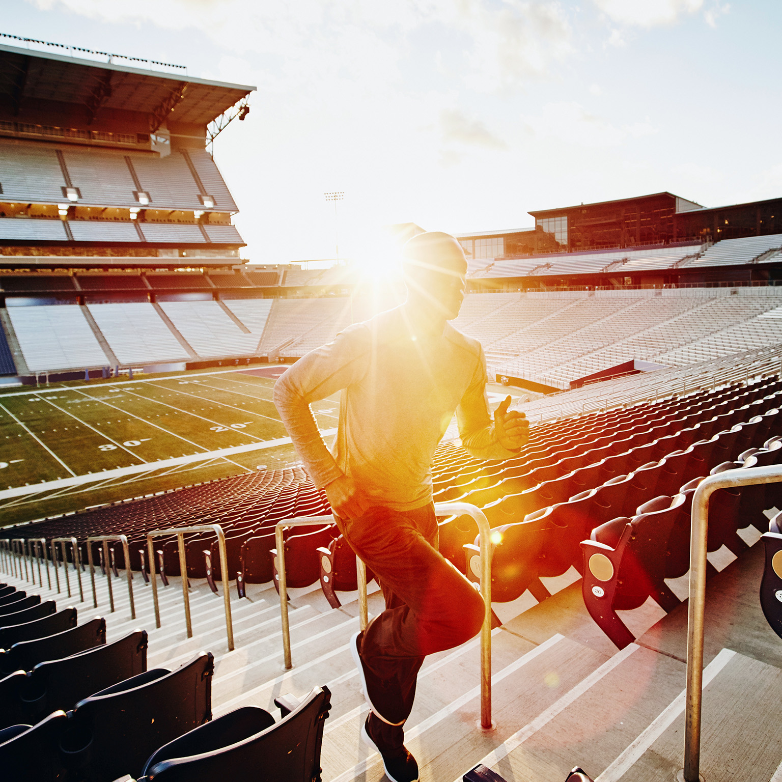 Male athlete running stairs during workout in empty stadium at sunset