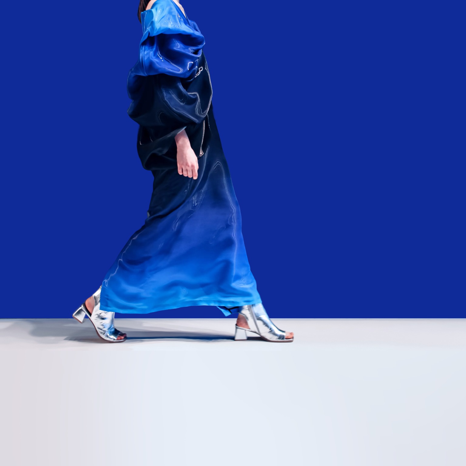 A woman struts down the runway in a creative blue designer satin dress