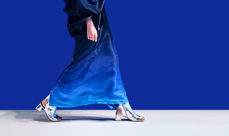 A woman struts down the runway in a creative blue designer satin dress