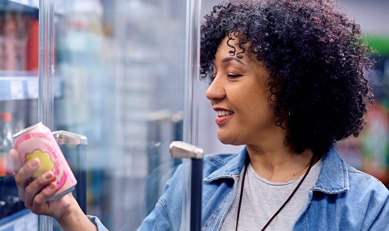 Happy woman holding a can of soda at refrigerated section in a supermarket