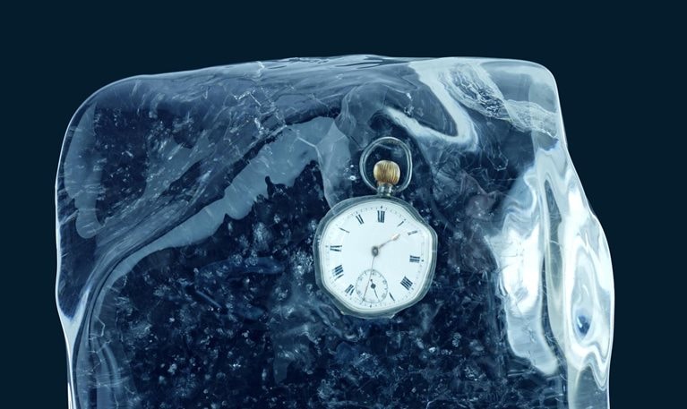 A pocket watch encased in a block of ice and set against a deep blue backdrop.